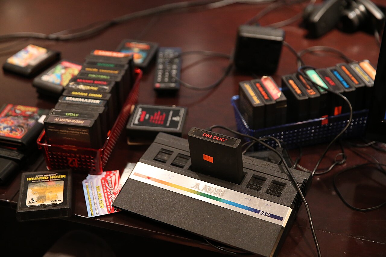 Une Atari 2600 avec une cartouche insérée, entourée d'une collection de cartouches de jeux classiques — Crédit : pxfuel (CC0, via Wikimedia Commons)