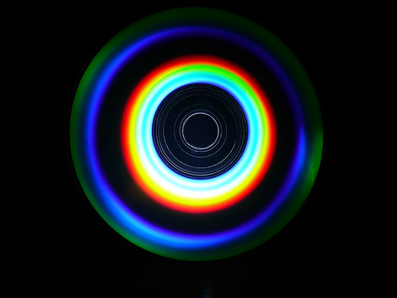 Anneaux de diffraction à la surface d'un CD. La spirale microscopique de creux qui encode la musique est aussi ce qui décompose la lumière blanche en ces anneaux arc-en-ciel. Crédit : Hapecko / Wikimedia Commons (CC BY-SA 4.0)