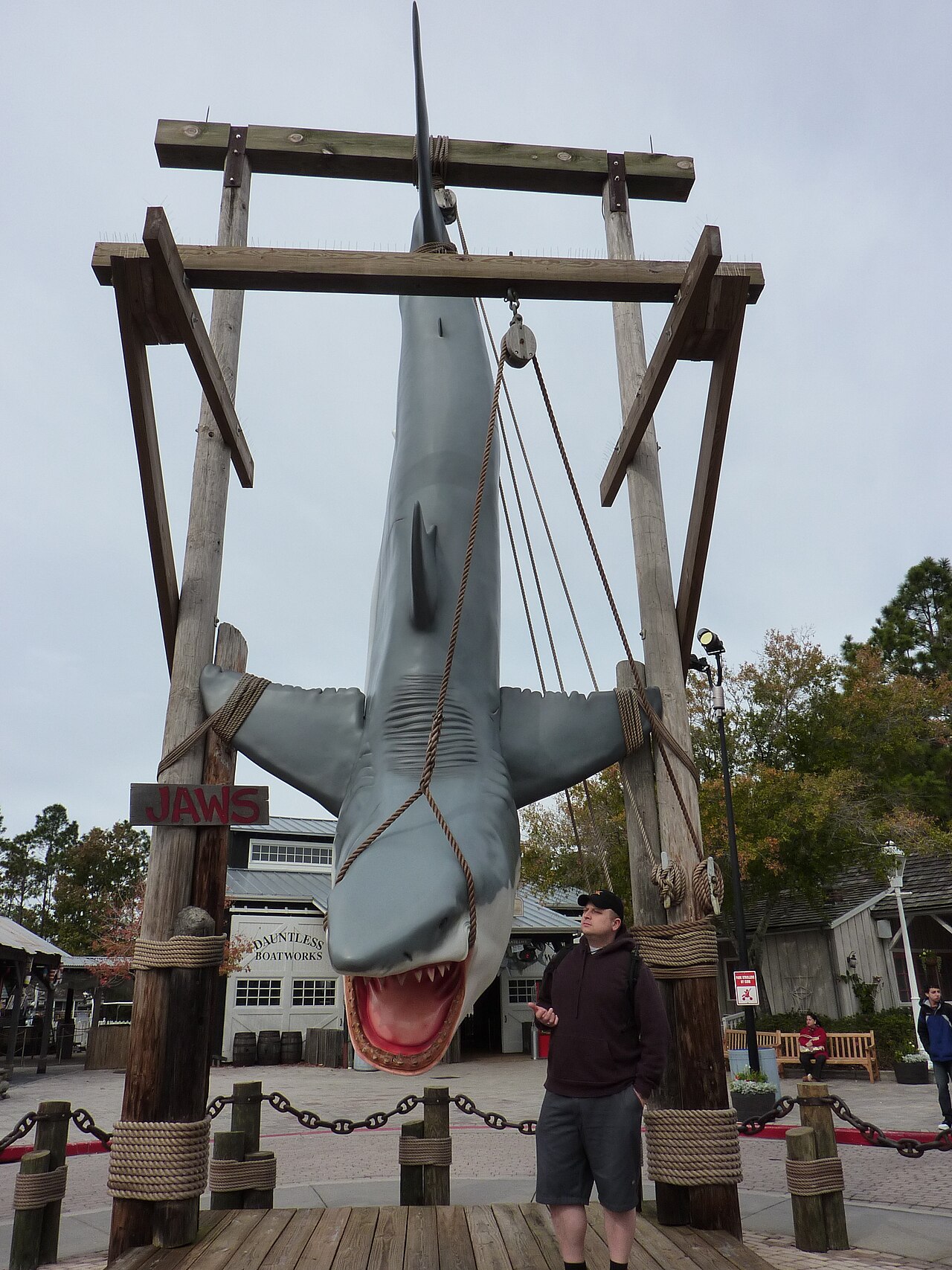 Bruce suspendu à l'ancienne attraction Jaws, une silhouette humaine donnant l'échelle — sept mètres de fibre de verre qui ont à peine survécu à un bassin d'eau douce. Crédit : cplbeaudoin, Wikimedia Commons (CC BY-SA 3.0)