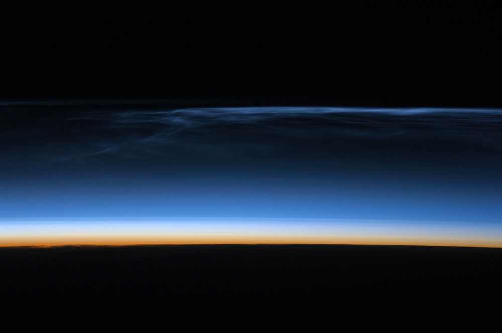 Des nuages noctulescents photographiés depuis la Station spatiale internationale, brillant comme une fine bande bleue au bord de l'atmosphère terrestre, au-dessus de l'Asie centrale. Crédit : NASA (domaine public).