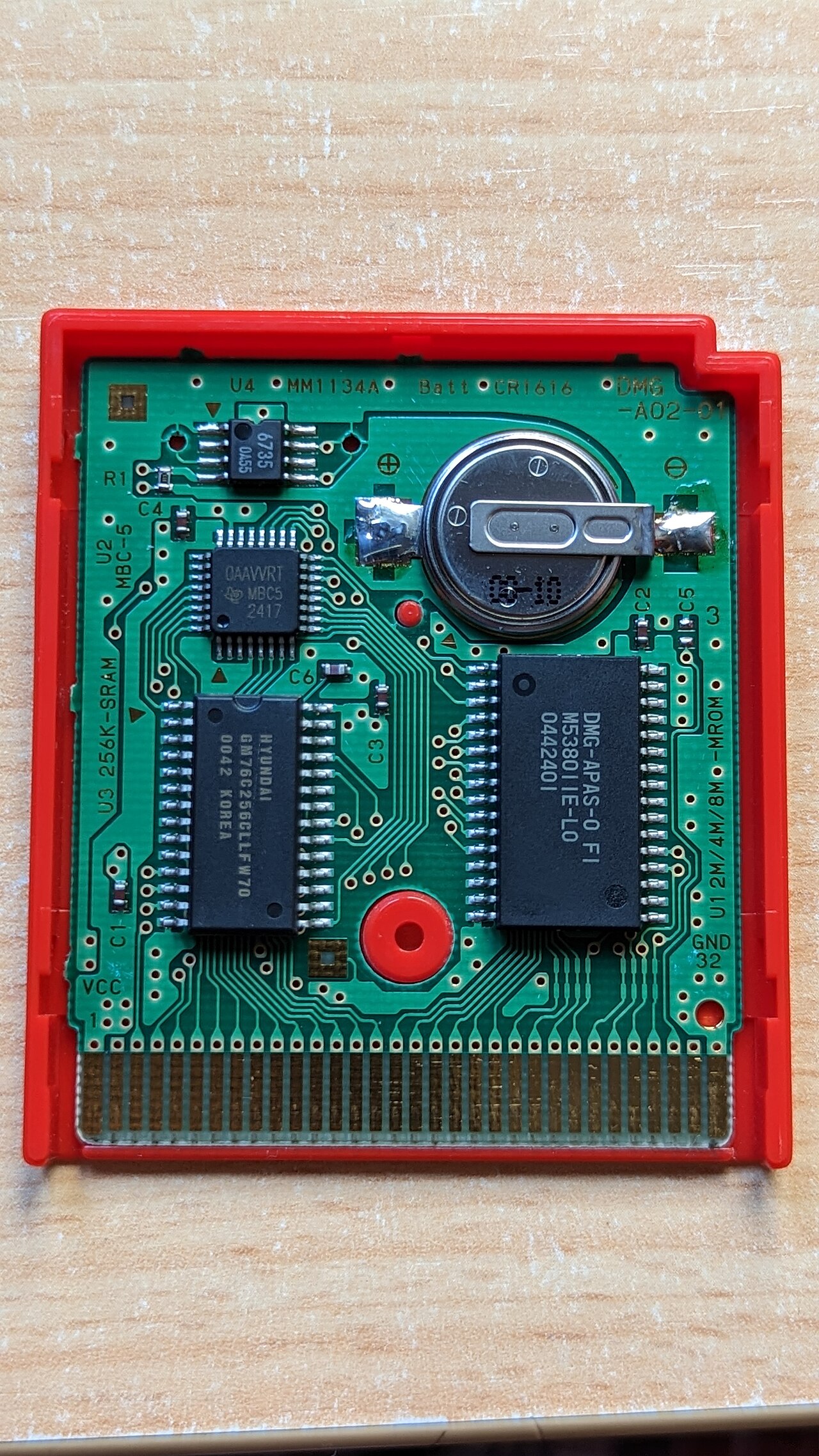 Le circuit imprimé à nu d'une cartouche Game Boy Pokémon — la grosse puce est la ROM qui stocke tout l'univers du jeu. Caser une seconde région, c'était en mettre une plus grande. — Crédit : MarianoBrajoy (CC BY-SA 3.0, Wikimedia Commons)