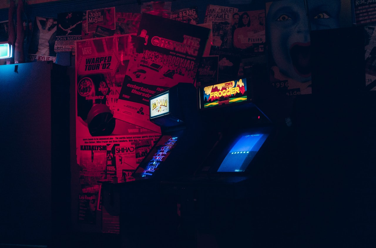 Deux bornes d'arcade lumineuses dans une pièce sombre tapissée d'affiches — l'ambiance inquiétante où vit Polybius. — Crédit : Ben Neale sur Unsplash (Licence Unsplash)